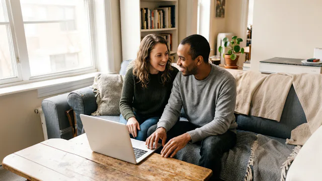 Stel zit samen op de bank in hun woonkamer met een laptop voor hen om de ideale cruise te boeken.