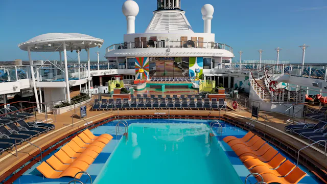 Zwembad op het dek van een cruiseschip met ligbedden, zonnedek en een groot scherm voor entertainment aan boord