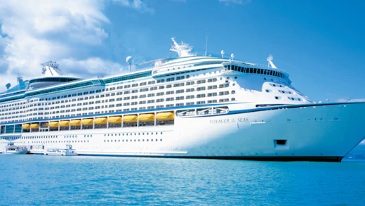 Luxe cruiseship op helderblauw water met een tropisch landschap en een deels bewolkte heel op de achtergrond.