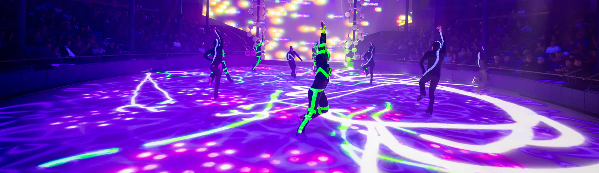 IC, Icon of the Seas, Ice Skaters performing at Absolute Zero while crowd watches, entertainment, performance, performers, show, lights, purple and green colors, day-glo green, arena,