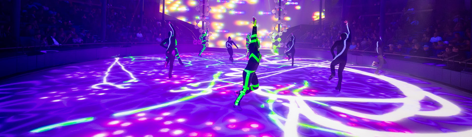 IC, Icon of the Seas, Ice Skaters performing at Absolute Zero while crowd watches, entertainment, performance, performers, show, lights, purple and green colors, day-glo green, arena,
