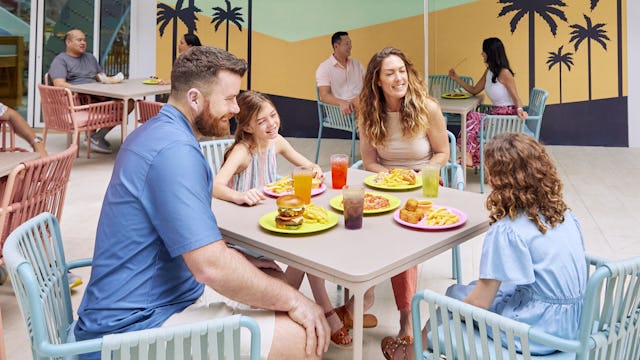 Family eating outside at Surfside Eatery onboard Icon of the Seas. Signage, family at table, casual dining, lunch.