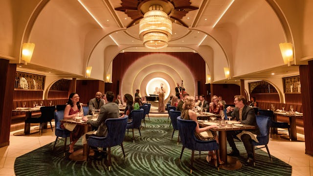 IC, dining room at Empire Supper Club onboard Icon of the Seas, wide shot, deco architecture, 1930s old New York theme, glamour, chandelier, jazz musicians on stage in the background, nightlife,