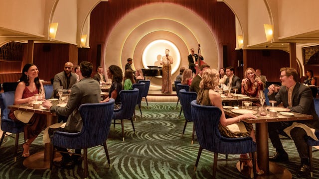 IC, dining room at Empire Supper Club onboard Icon of the Seas, wide shot, deco architecture, 1930s old New York theme, glamour, chandelier, jazz musicians on stage in the background, nightlife,