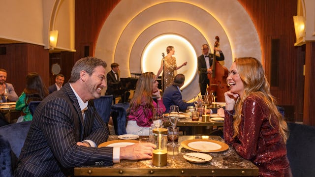 IC, Couple dining at Empire Supper Club onboard Icon of the Seas, musical group on stage in the background, nightlife, fun, evening, 1930s old New York theme, glamour,