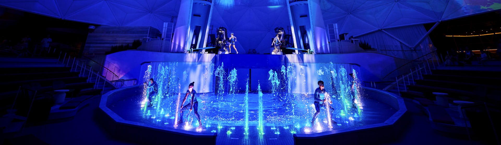 IC, Icon of the Seas, wide shot of performers, on stage in AquaTheater show. Aqua Action, fountains of water bubbling up, excitement, exciting, blue colors, stage lights,
