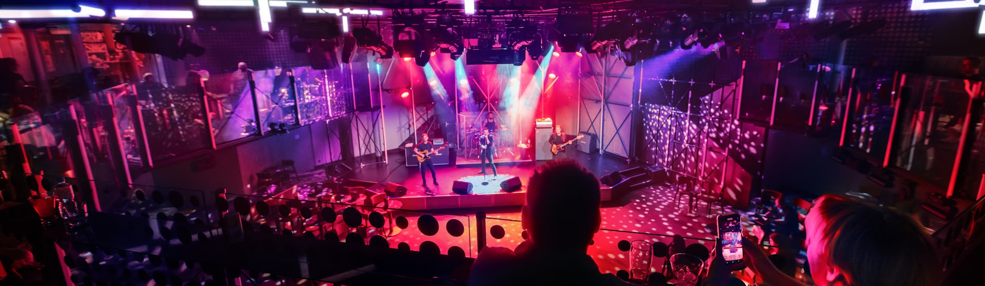 IC, Icon of the Seas, two people in audience looking down at live band playing at the Music Hall, performance, red colors,