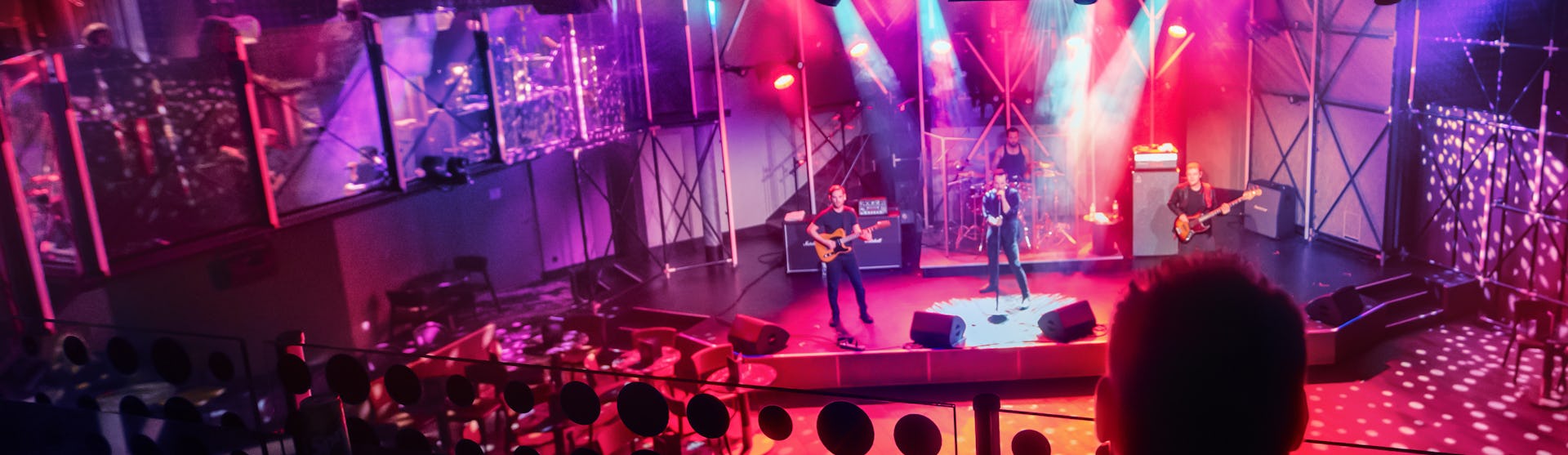 IC, Icon of the Seas, two people in audience looking down at live band playing at the Music Hall, performance, red colors,