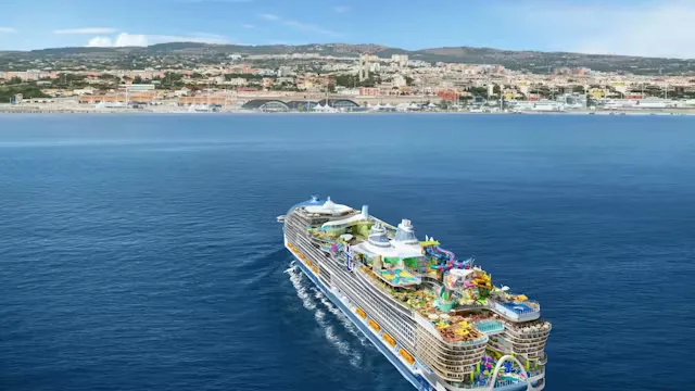 Groot Royal Caribbean-cruiseschip vaart over helderblauw water richting een kuststad op een zonnige dag.