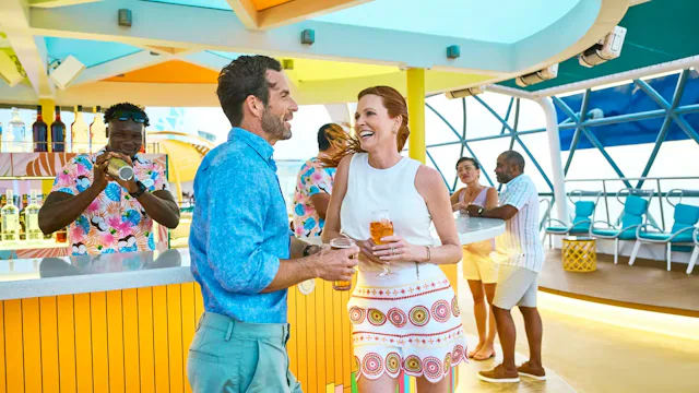 Vrolijke gasten genieten met drankjes in de hand bij een kleurrijke buitenbar op het dek van een cruiseschip.