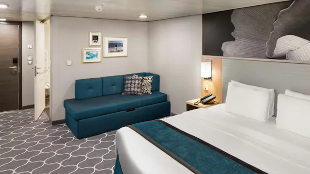 Moderne cruisehut met een tweepersoonsbed, blauwe bank, nachtkastje en zachte verlichting aan boord van een cruiseschip.