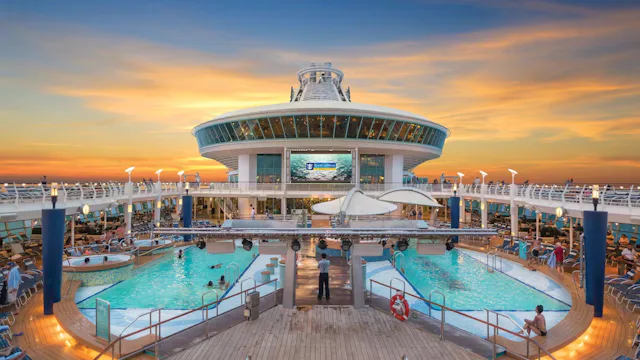 Zwembaddek op een Royal Caribbean-cruiseschip bij zonsondergang, met twee zwembaden, ligstoelen en uitzicht over zee.