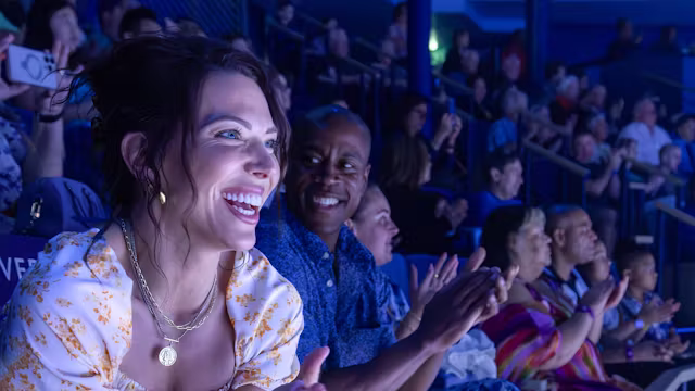 Vrolijke gasten genieten van een show in een theater op een cruiseschip en applaudisseren vanaf hun zitplaatsen. 