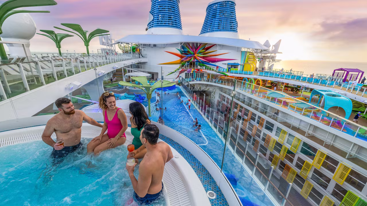 Vier gasten ontspannen met drankjes in een bubbelbad op het zonnedek van een cruiseschip, met uitzicht op het zwembad en kleurrijke waterattracties.