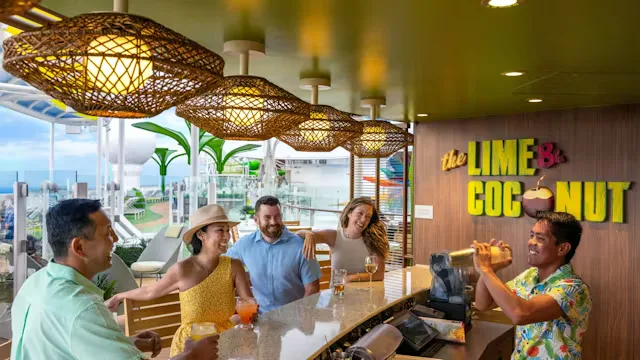 Gasten zitten aan de bar en genieten van drankjes in een kleurrijke buitenruimte op een cruiseschip met uitzicht op het dek.