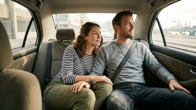 Stel zit ontspannen op de achterbank van een taxi op weg naar huis na een cruise, terwijl ze door het raam naar buiten kijken.