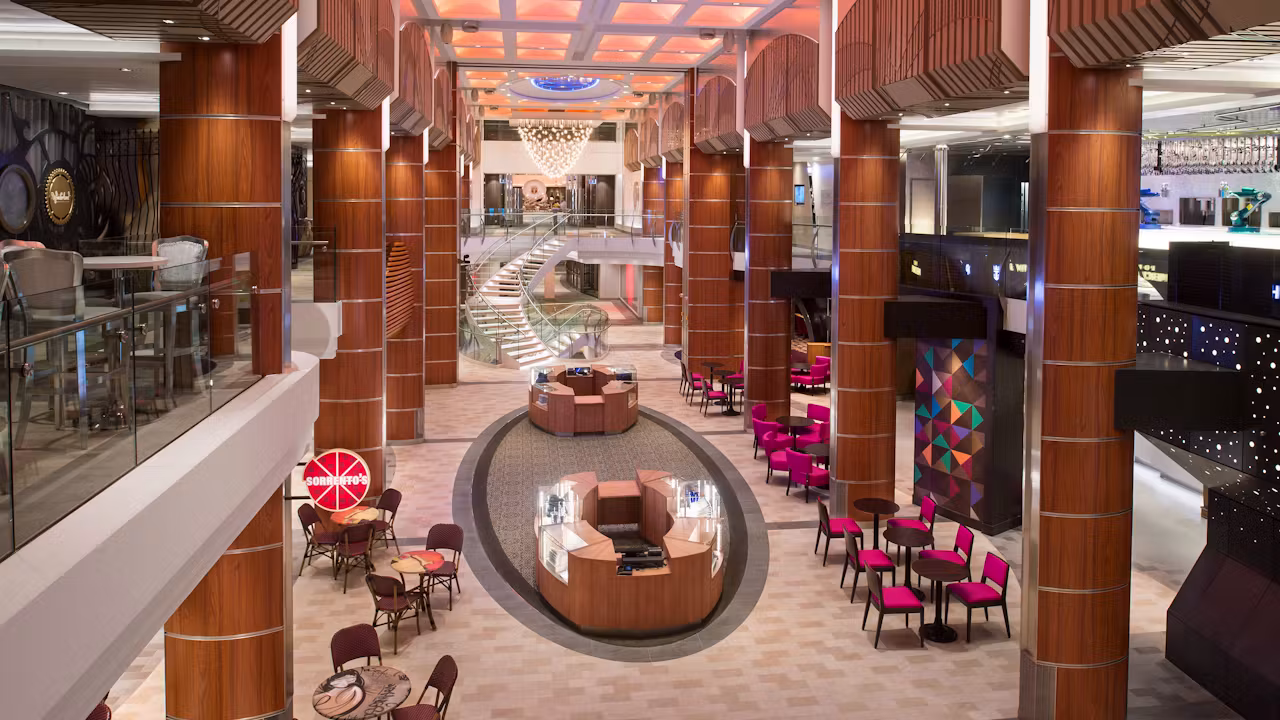 Ruime en moderne promenade aan boord van een cruiseschip met winkels, zitplekken, trappen en een stijlvolle, luxe uitstraling.