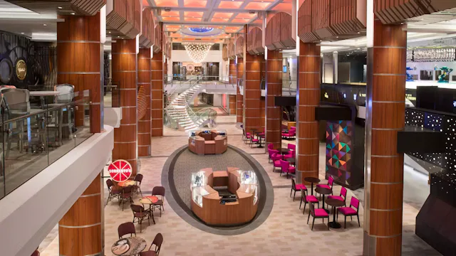 Ruime en moderne promenade aan boord van een cruiseschip met winkels, zitplekken, trappen en een stijlvolle, luxe uitstraling.